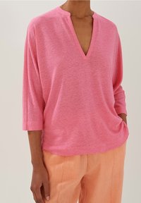 Rosa kortärmad topp med V-hals och avslappnad passform, tillverkad av mjukt material. Matcher med ljusorange linnebyxor.