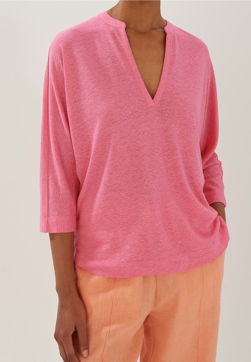 Rosa kortärmad topp med V-hals och avslappnad passform, tillverkad av mjukt material. Matcher med ljusorange linnebyxor.