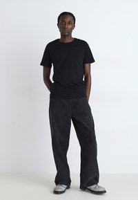 T-shirt noir à col rond, pantalon en denim large foncé et baskets grises. Tissu lisse, coupe décontractée, design simple sans motifs ni accents visibles.