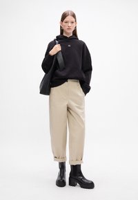 Felpa nera con cappuccio, pantaloni beige su misura e stivali neri con tacco spesso alla caviglia. L'outfit presenta un design minimalista e colori a contrasto.