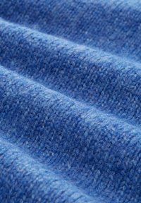 Gewebter blauer Stoff mit einer weichen Textur, der ein subtilmuster aus erhabenen und flachen Bereichen zeigt und dadurch Tiefe und visuelles Interesse erzeugt.