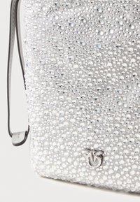 Silberne Tasche, die mit klaren Strasssteinen bedeckt ist, mit glatter Textur, verstellbarem Tragegurt und einem kleinen metallischen Logo-Akzent am Boden.