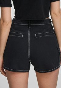 Shorts in denim nero con cuciture bianche a contrasto, caratterizzati da una vita alta, tasche posteriori e orli arrotolati. Il materiale sembra robusto e con una consistenza interessante.