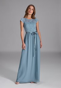 Langes, blaues Kleid mit einem Spitzenoberteil, schuppenförmigen Ärmeln und einem Satinschal um die Taille. Flüssiger Rock mit einer sanften Textur.