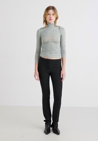 Lys grønn, langermet cropped topp med rynket tekstur, sammen med svarte smale bukser og spisse svarte sko.