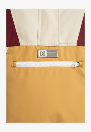 DC-jack met een bordeauxrode en crèmekleurige bovenkant en een gele ondersectie. Bevat een horizontale witte ritszak en een merklabel.