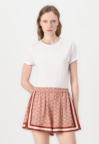 Balti trumpa rankovė t-shirt su raštuotomis persikų spalvos šortais, kurie turi geometrinį raštą ir elastingą juosmenį su kontrastingais šoninėmis detalėmis.