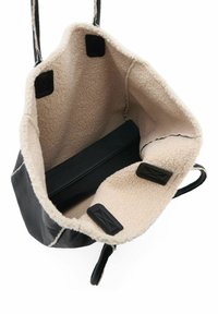 Sac fourre-tout en cuir noir avec un intérieur en polaire beige doux. Il dispose d'un fond plat et de poches latérales, avec des poignées en tissu noir.