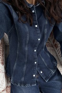 Dark denim jacket with a button-up front, white buttons, and vertical seams. Features a classic collar and textured fabric.