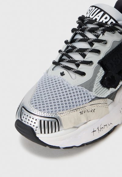 Sneaker gri cu elemente din plasă și piele, accente argintii, suprafață texturată, șireturi negre și un eticheta evidențiată pe lateral.