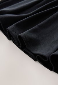 Tissu en coton noir, plié avec des coutures visibles. Texture lisse et tombé uniforme, mettant en valeur sa qualité douce et souple.