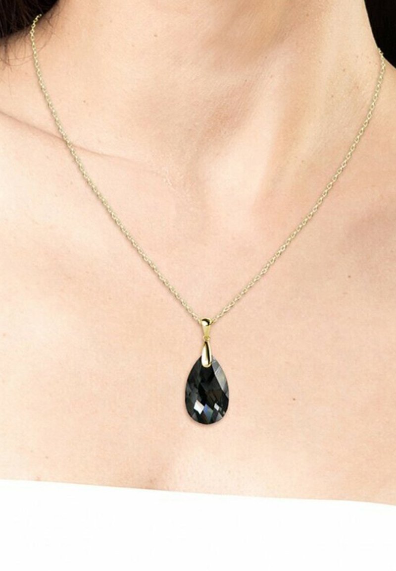 Collana in oro con un ciondolo in pietra nera a forma di pera con superficie sfaccettata, appoggiata su pelle nuda.