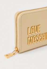 Μπεζ πορτοφόλι με φερμουάρ και ανάγλυφα χρυσά γράμματα «LOVE MOSCHINO», με απαλό υλικό και μεταλλικό φερμουάρ.