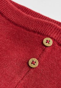Red knitted sweater featuring a ribbed collar, two gold buttons with engraved text, and a textured weave.