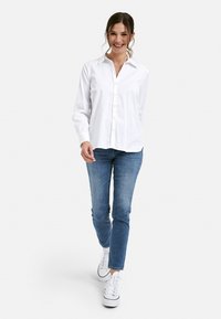 White button-up shirt, long sleeves, relaxed fit, paired with blue jeans and white sneakers. Smooth texture, classic collar design.