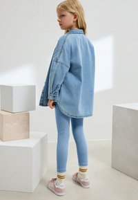 Oversized skjorte i lyseblå denim med lange ærmer. Kombineret med ribstrikkede lyseblå leggings, pink sneakers og stribede sokker.