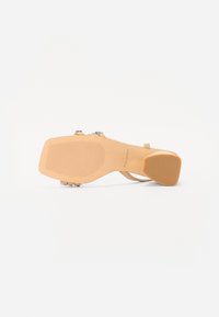 Beige høyhælte sandaler med teksturert såle, prydet med klare krystalldetaljer på remmene. Har en avrundet hæl og et minimalistisk design.