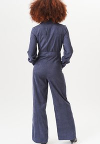 Denim jumpsuit in dark blue with long sleeves, a fitted waist, and wide-leg pants, featuring a collar and back seam detailing.