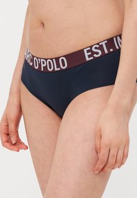 Tamno plavi gaćice s bordo elastičnim pojasom na kojem se nalazi bijeli tekst. Čini se da je materijal mekan i glatke teksture, osmišljen za udobnost.