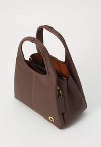 Bolso de mano marrón de piel con asas dobles, herrajes dorados y una etiqueta de piel colgante, mostrado sobre un fondo blanco.
