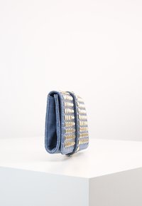 Světlomodrá peněženka z umělé krokodýlí kůže s pozlacenými kovovými hroty, obdélníkový tvar a texturovaný povrch. Kompaktní a zavřený design.