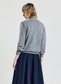 Leichter grauer Strickpullover mit strukturiertem Rautenmuster, Rundhalsausschnitt und gerippten Bündchen, kombiniert mit einem dunkelblauen fließenden Rock.