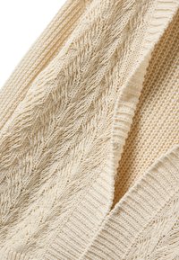 Gebreid vest in crème, met textuurrijke patronen en geribbelde randen. De stof is zacht, met een open voorkant en subtiele details.