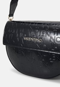 Borsa a tracolla in pelle nera con lettere in rilievo, dettaglio logo dorato e design con patta curva. Texture liscia con finitura lucida.