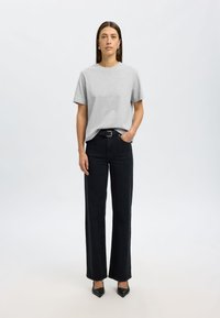 Camiseta de algodón gris con mangas cortas, combinada con jeans negros rectos y tacones de punta negros, con un cinturón simple.