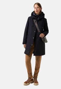 Granatowy wodoodporny parka z puchowym kapturem, z zapięciem na zamek błyskawiczny i napy, w połączeniu z beżowymi dresami i brązowymi butami górskimi z koronkami.