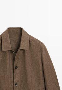 Manteau en laine avec chevrons marron, col large et boutons noirs, présenté de face sur un fond blanc.