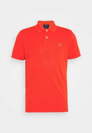 Polo rouge vif à manches courtes avec deux boutons blancs et un petit logo GANT sur le côté gauche de la poitrine.