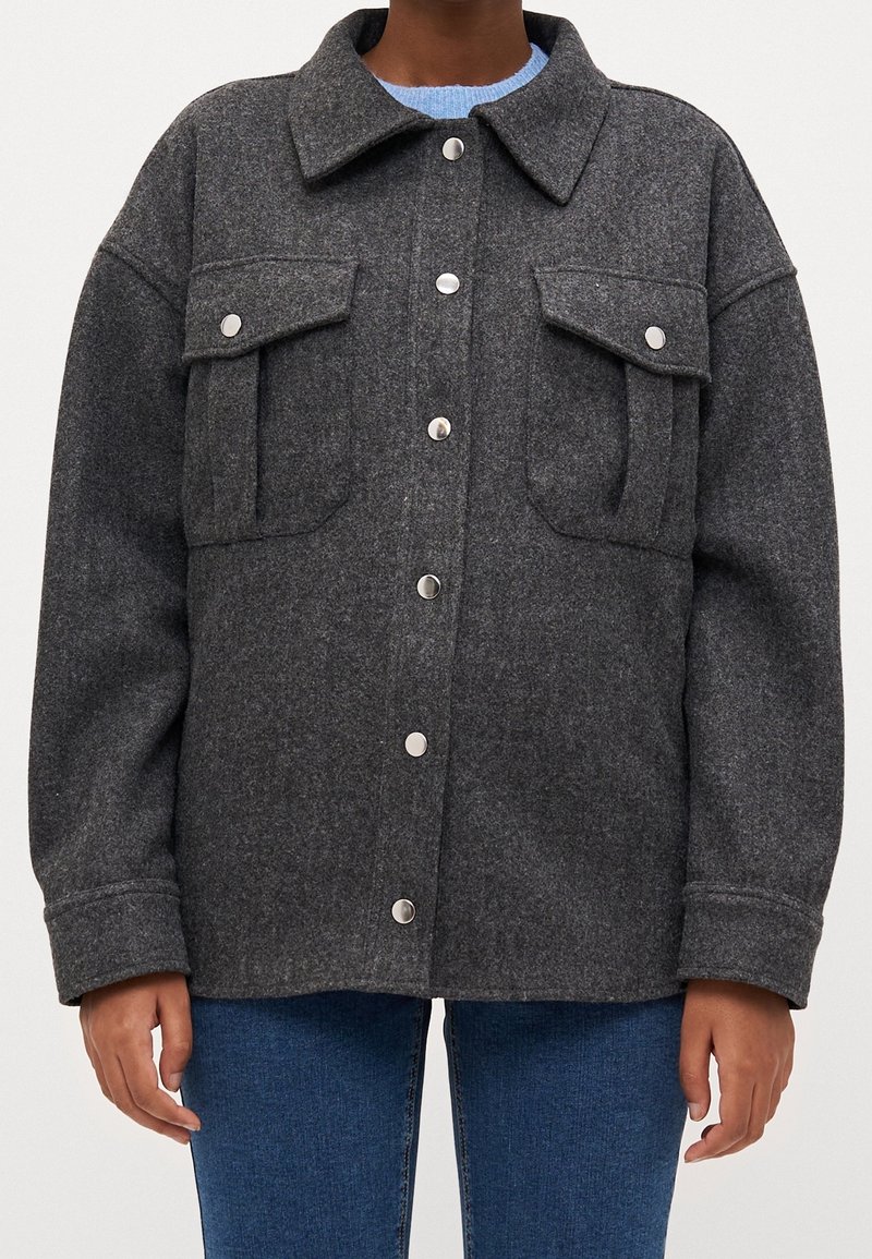 Szary żakiet z wełny z domieszką, z zapinanym przodem, dwoma kieszeniami na piersi, kołnierzykiem oraz zapięciem na zatrzaski. Luźny krój z długimi rękawami.