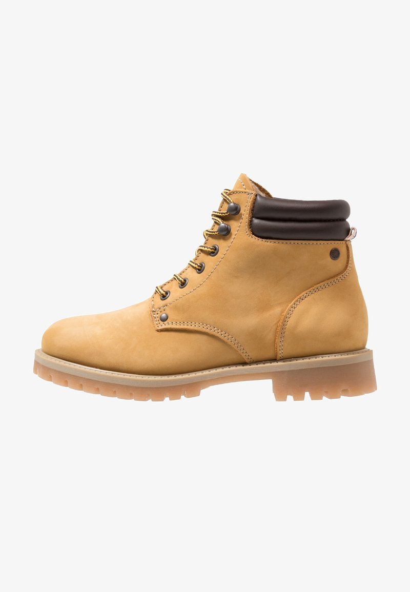 Botte de travail en cuir couleur fauve avec lacets, col de cheville rembourré marron foncé et semelle épaisse en caoutchouc avec des crampons profonds, vue de côté.