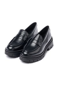 Mocasines de cuero negro con punta redondeada, costuras prominentes y una suela de goma gruesa que presenta un patrón de agarre.