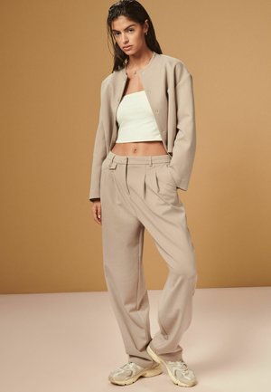 Beige rövidített dzseki és hozzáillő, magas derekú nadrág, puha anyagból, laza szabással. Fehér crop top alatta. Világos színű sportcipők.