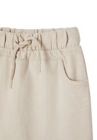 Beige Jogginghose mit einem elastischen Bund, verstellbarem Kordelzug und einer Seitentasche. Der Stoff ist weich mit einer glatten Textur.