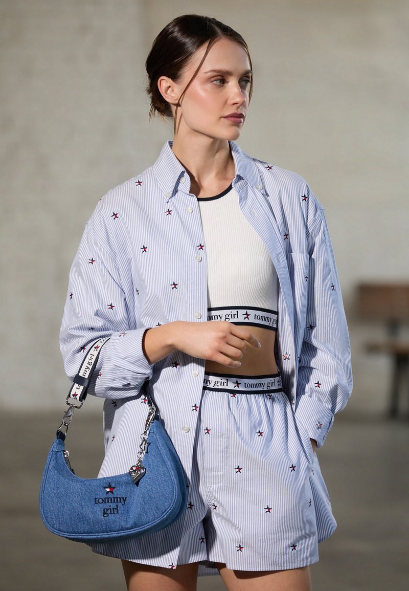 Modra in bela črtasta majica z rdečo vezenino zvezde, v kombinaciji z belo krajšo majico in ujemajočimi se hlačami. Drži denim torbico z logotipom.