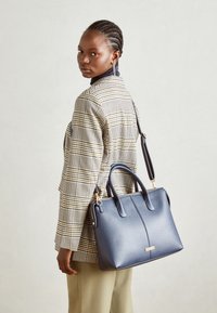 Skórzana granatowa torebka o eleganckim designie, z podwójnymi uchwytami u góry, odpinanym paskiem na ramię oraz subtelnymi detalami metalowymi.