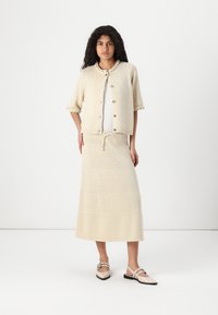 Ensemble de cardigan tricoté et jupe assortie dans une teinte crème clair, présentant un tissu texturé, un col rond et des boutons décoratifs.