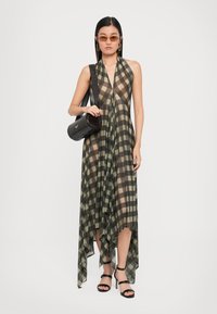 Long, sheer dress in green and brown check pattern with a high-low hem. Paired with strappy black heels and a round black bag.