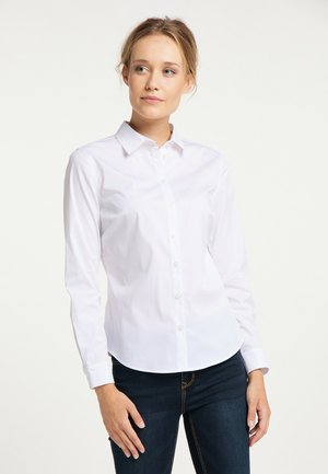 Witte langlijfshirt van zachte katoen met een knoopsluiting aan de voorkant, spitse kraag en een gebogen onderrand, gecombineerd met donkere spijkerbroek.