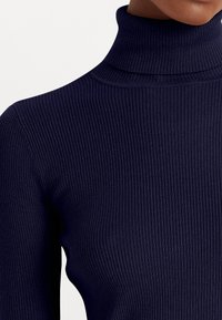 Marinblå ribbad polotröja med ett strukturerat mönster, som har hög hals och figursydd design. Slät tyg med lätt lyster.