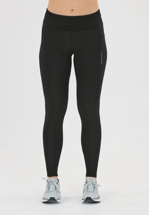 Zwarte high-waisted leggings van rekbaar materiaal, met een zijzak en platte naden. Gecombineerd met lichtgrijze sportschoenen.
