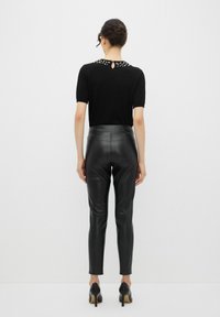 Zwarte top met korte mouwen en decoratieve kraaldetails bij de halslijn, gecombineerd met aansluitende zwarte faux leren broek en zwarte hoge hakken.