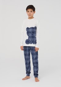 Zestaw piżamowy dla dzieci składający się z białej bluzki z długim rękawem z niebieskim w kratkę wzorem misia oraz pasujących granatowych spodni w kratkę.