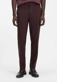 Bordeauxrote, maßgeschneiderte Hose mit glatter Textur, ausgestattet mit geradem Bein, flacher Vorderseite und Gürtelschlaufen, kombiniert mit schwarzen Schuhen.