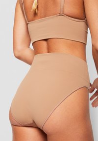 Hochgeschnittene Unterhose in einem hellen Braunton, hergestellt aus glattem Stoff mit subtilen Nahtdetails. Verfügt über einen weichen Bund für zusätzlichen Komfort.