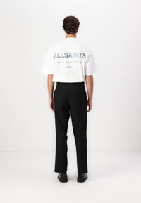 Vit kortärmad t-shirt med "ALLSAINTS" och japansk text på baksidan, tillsammans med svarta skräddarsydda byxor och svarta skor. Enkelt, rent design.