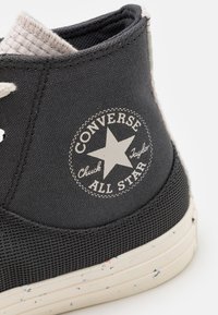 Nahaufnahme eines schwarzen Converse Chuck Taylor All Star Sneakers, der das strukturierte Gewebe, das weiße Sternlogo-Patch und die gesprenkelte weiße Gummisohle zeigt.
